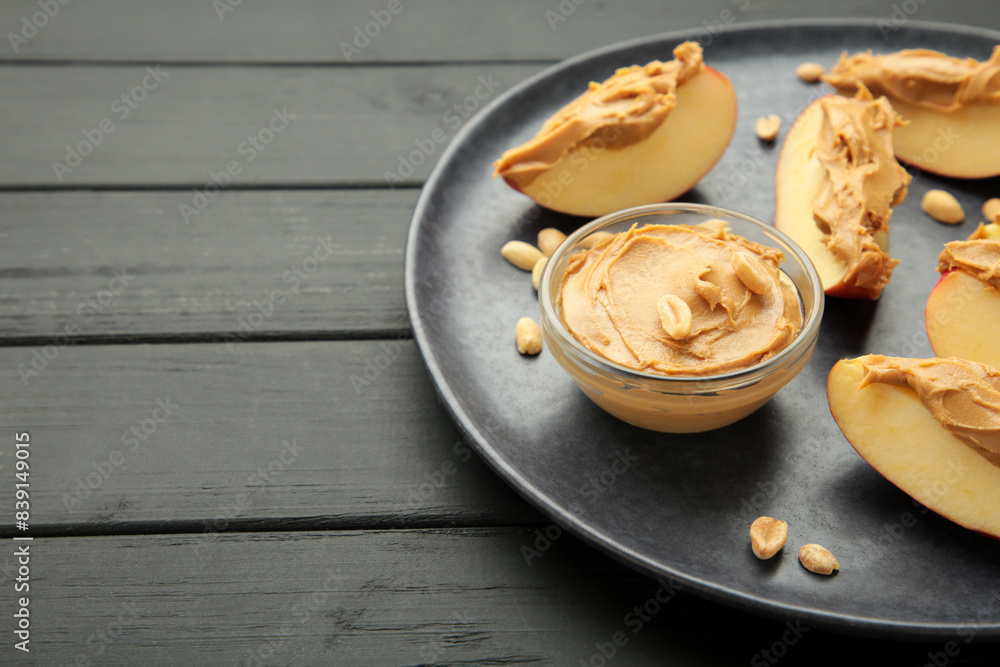 Slices of fresh apple with peanut butter in bowl on mint plate on black wooden background. Slices of fresh apple with peanut butter in bowl on mint plate on black wooden background.