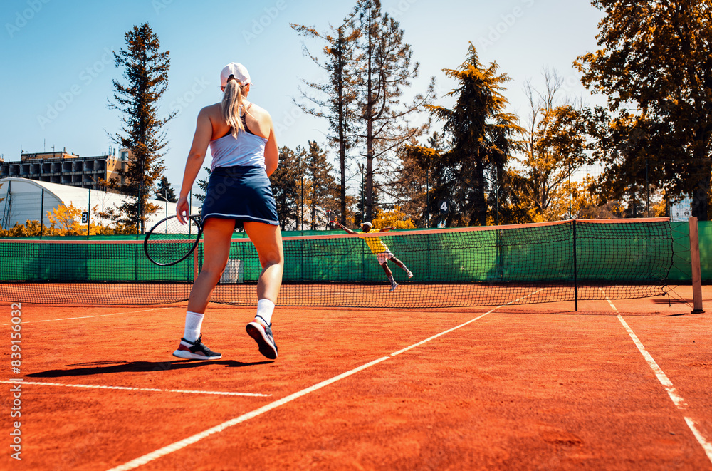 Obraz premium Couple playing recreational tennis on a clay court during the day.