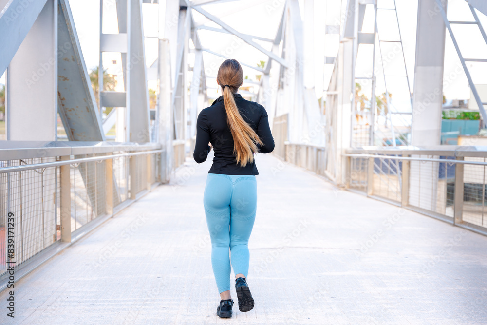 Obraz premium Rear view a young runner with water bottle in hand trains around the city.