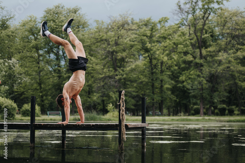 Photography Young man performing a handstand on a pier beside a calm lake surrounded by lush