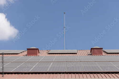 A roof with  dirty solar panels on it and a pole in the middle © Rattanachat