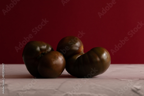 Tomate kumato sobre mesa blanca con fondo rojo