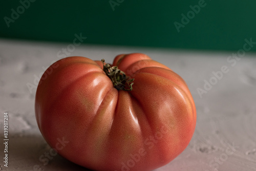 Tomate rosa sobre mesa blanca con un fondo verde.