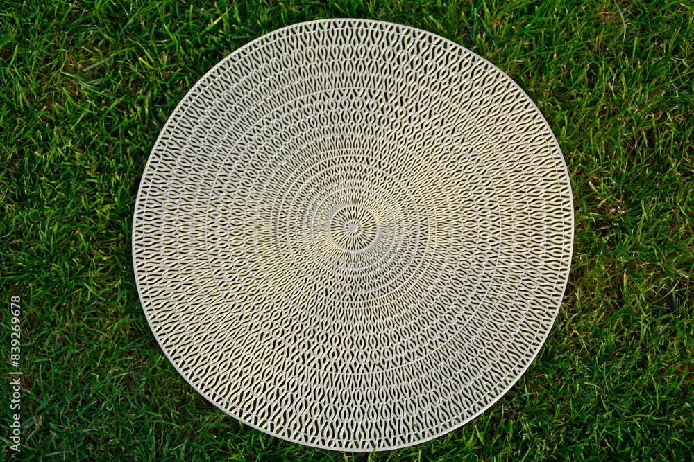 Fototapeta premium ażurowy wzór, złota podkładka na stół na tle trawnika, wzór mandala, gold table mat, mandala pattern, Decorative Doily, Gold table mat surface as background, closeup 