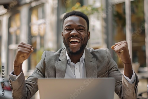 Happy businessman sitting, using laptop at table gesturing fist