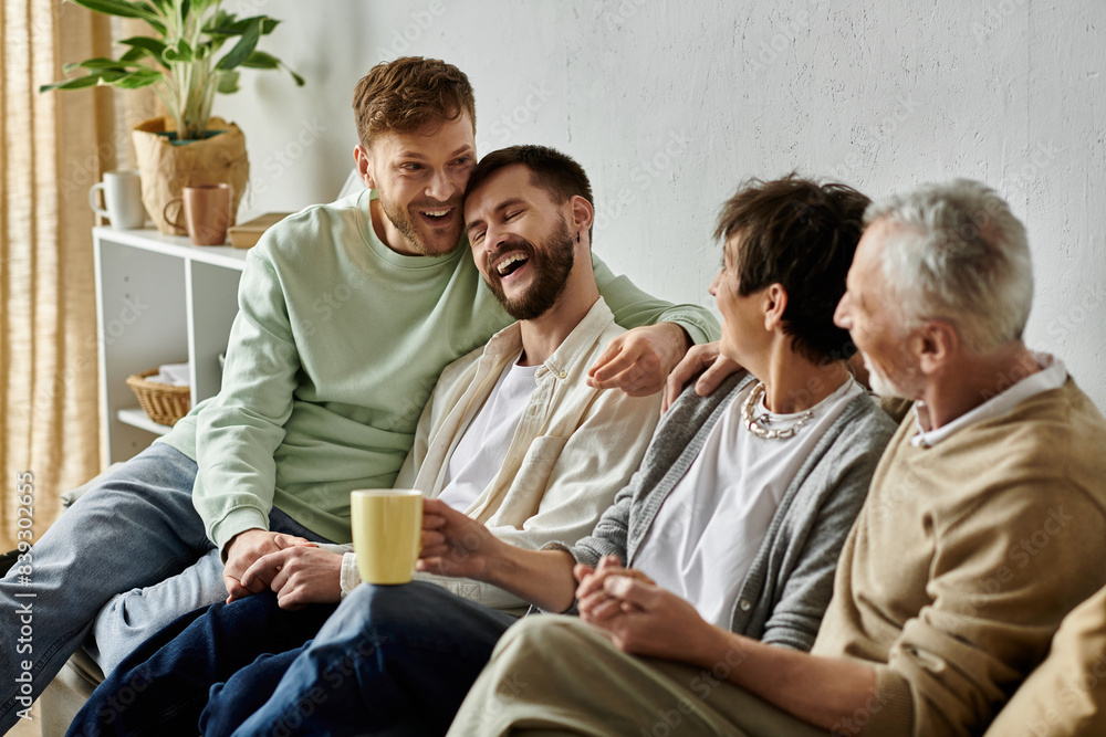 A gay couple sits with parents on a couch, laughing and enjoying a relaxed moment together. A gay couple sits with parents on a couch, laughing and enjoying a relaxed moment together.