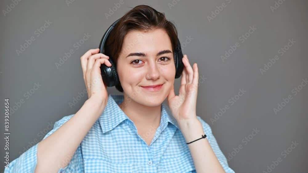 Young woman in headphones dancing on gray background