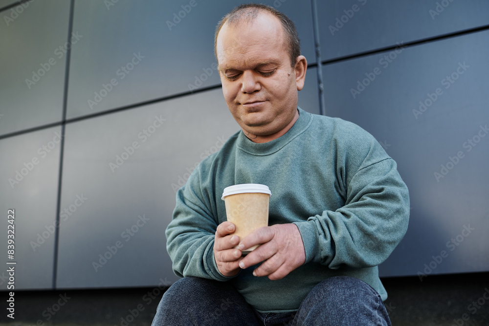 A man with inclusivity sits outside, thoughtfully holding a cup of coffee. A man with inclusivity sits outside, thoughtfully holding a cup of coffee.