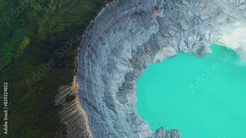 Panoramic drone view of turquoise sulfur water lake, surrounded by rock cliff at Kawah Ijen volcano. Aerial perspective in East Java, Indonesia. Natural landscape background
