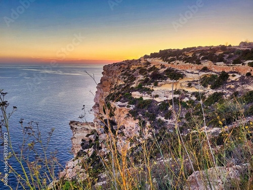 Beautiful landscape with blue sea and rocky shore. Tropical beach with ocean and rocky cape in island. Sun beyond the headland with glowing marsala toned rocks in the foreground. Beauty world photo