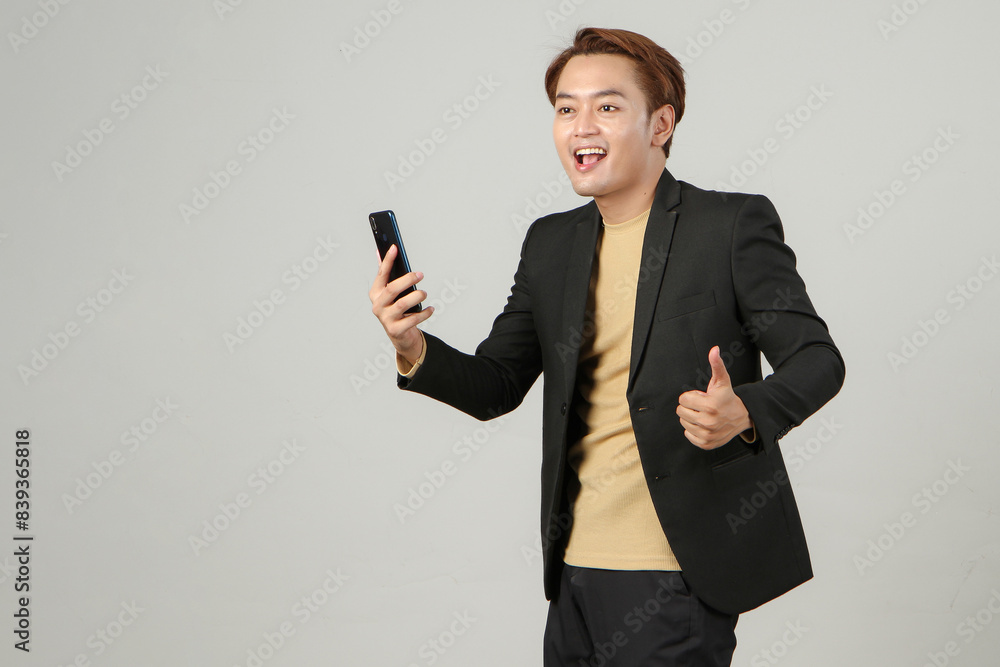 portrait of happy asian businessman wearing suit holding mobile phone giving thumb up gesture on isolated background. portrait of happy asian businessman wearing suit holding mobile phone giving thumb up gesture on isolated background.