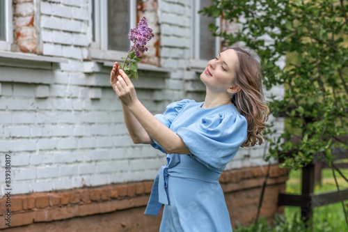 A beautiful girl, a brunette hair in a blue dress, walks in a lilac garden, a peasant woman in the village