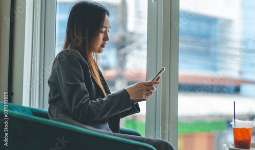 Asian young beautiful happy professional successful businesswoman designer sitting smiling at workstation desk using laptop notebook computer and smartphone working remotely online at home office