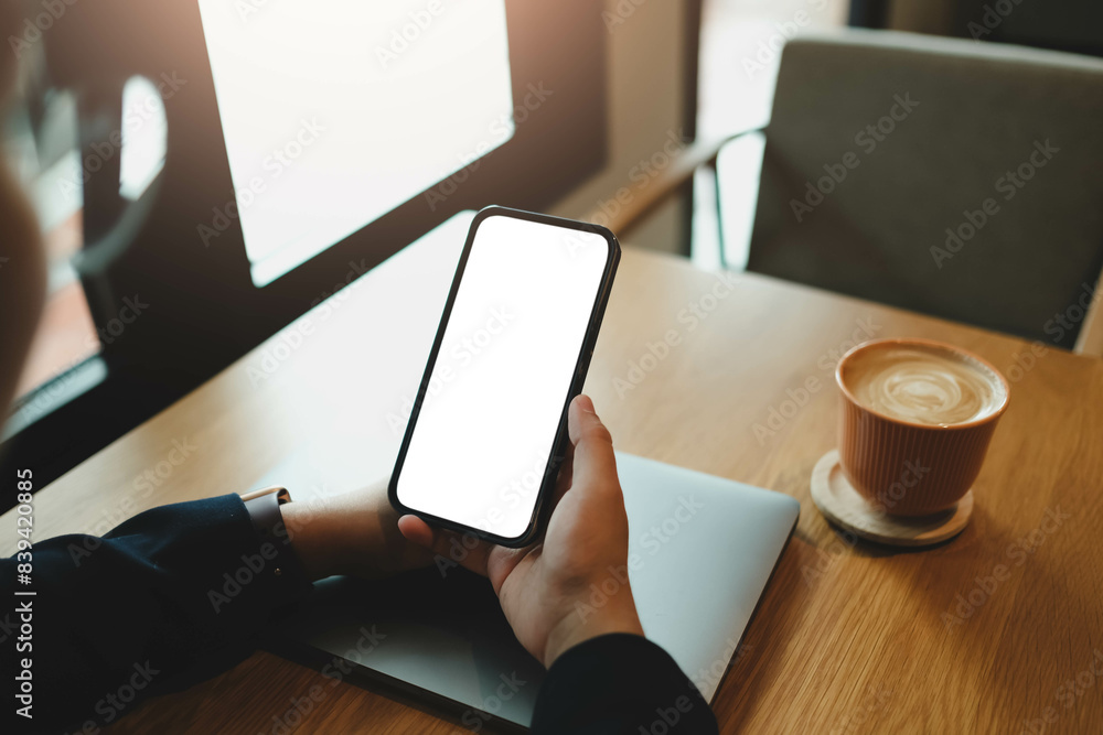 Naklejka premium A Woman Holding Smartphone with Blank Screen, Laptop, and Coffee on a Café Table.