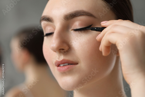 Makeup product. Woman applying black eyeliner on blurred background, closeup
