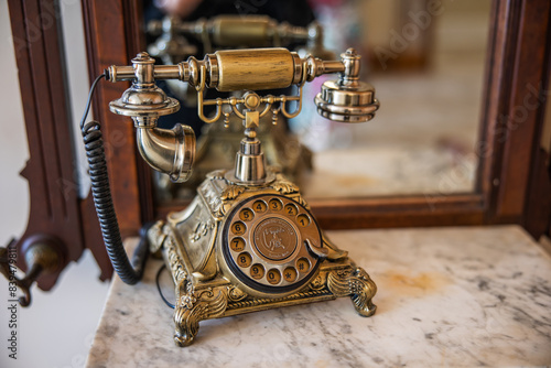 An old vintage antique gold dial up telephone for communication sitting on a marble dresser with a mirror