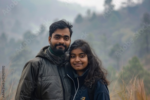 Portrait of a tender indian couple in their 20s wearing a windproof softshell while standing against quiet countryside landscape