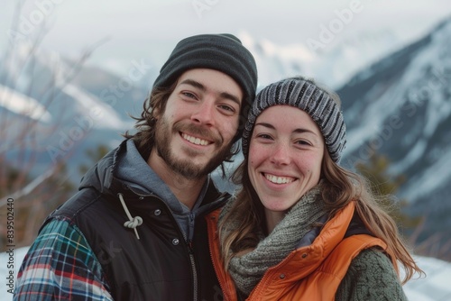 Portrait of a grinning couple in their 20s dressed in a thermal insulation vest while standing against backdrop of mountain peaks