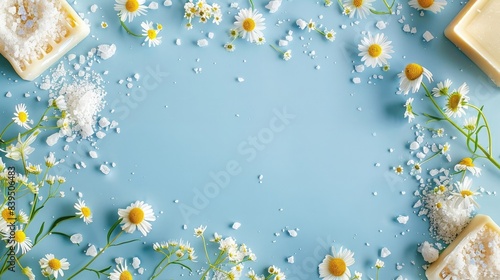A spikey frame made of soap, salt, and body powder with chamomile flowers on a blue background in a top view flat lay copy space.