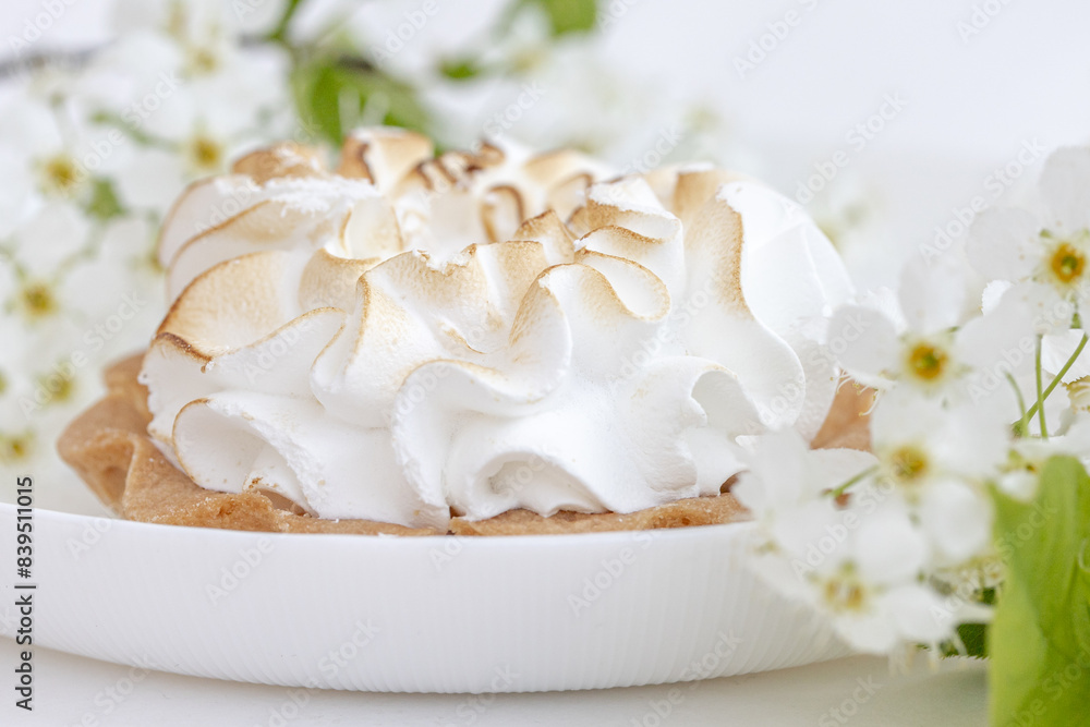 Delicious tartlet with meringue on a white plate, a branch of blooming cherry tree. Sweet treat in spring or summer, copy space Delicious tartlet with meringue on a white plate, a branch of blooming cherry tree. Sweet treat in spring or summer, copy space