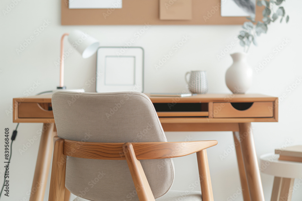 Fototapeta premium Clean and bright home office space featuring a natural wood desk and a comfortable looking chair. The desk is decorated with a lamp, a vase and office supplies