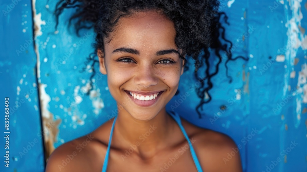 Woman with curly hair smiles brightly against a blue wall Woman with curly hair smiles brightly against a blue wall
