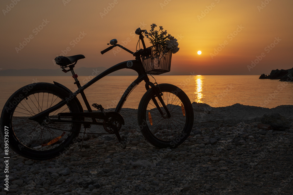 Obraz premium A bicycle with flowers against the background of a spectacular sunset on a hot summer evening in Greece.
