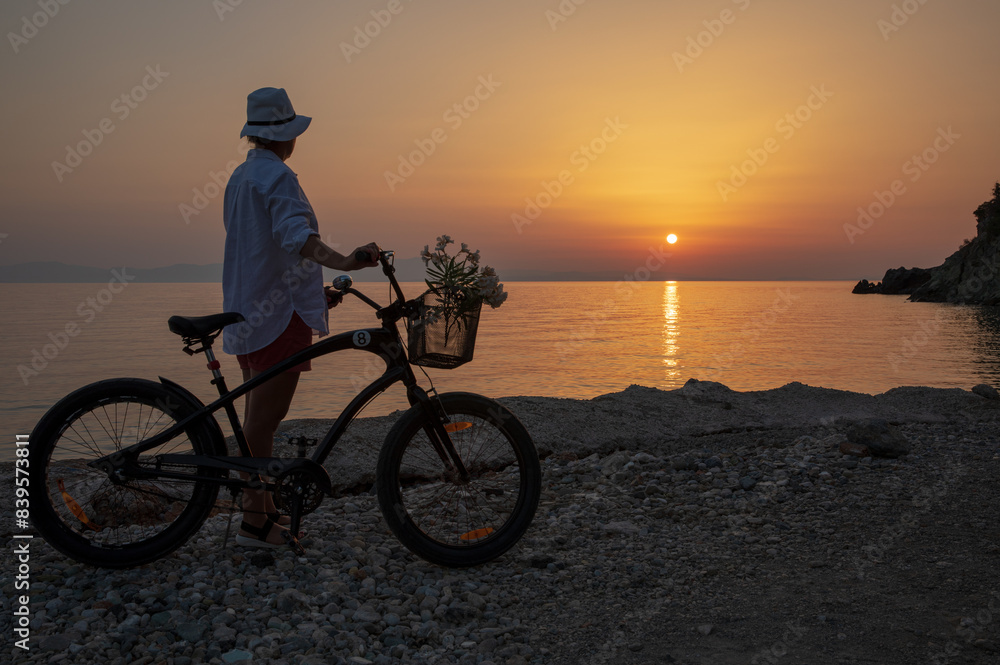 Fototapeta premium A young woman with a bicycle enjoys the sunset by the sea. 