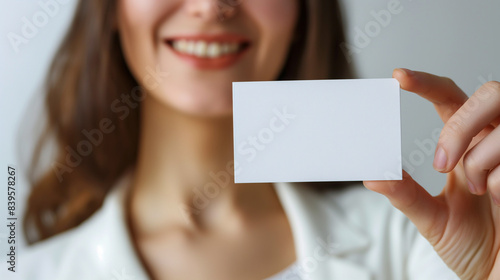 Business card. Casual young and attractive businesswoman showing her blank white business card / empty sign. Mixed race model isolated on seamless white background.