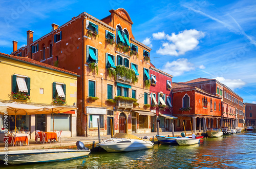 Murano Island in Venice, Italy. Antique age-old italian house on the channel with motorboats. Blue sky and white clouds murano. Sunny summer day. Popular touristic travel destination Europe
