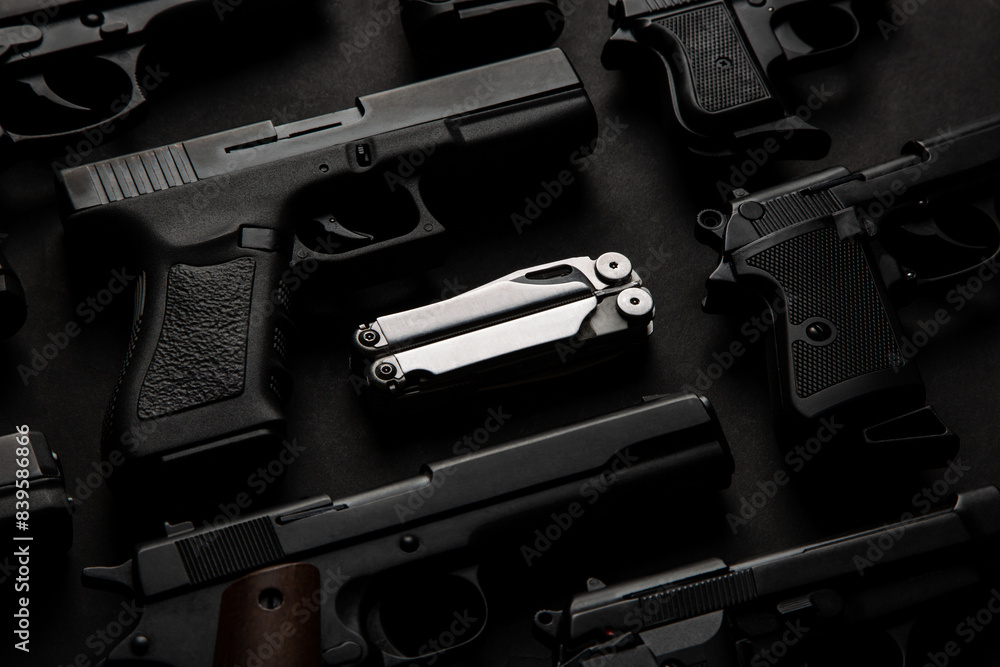 Silver multi-tool among various semi-automatic pistols. Dark back Silver multi-tool among various semi-automatic pistols. Dark back