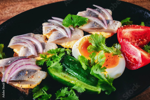 Herring sandwiches with rye bread, onion. Vegetable slicing, eggs, tomato, cucumber, parsley on plate. Smorrebrod toast with bread, herring and onion. Restaurant dish, seafood. Close up