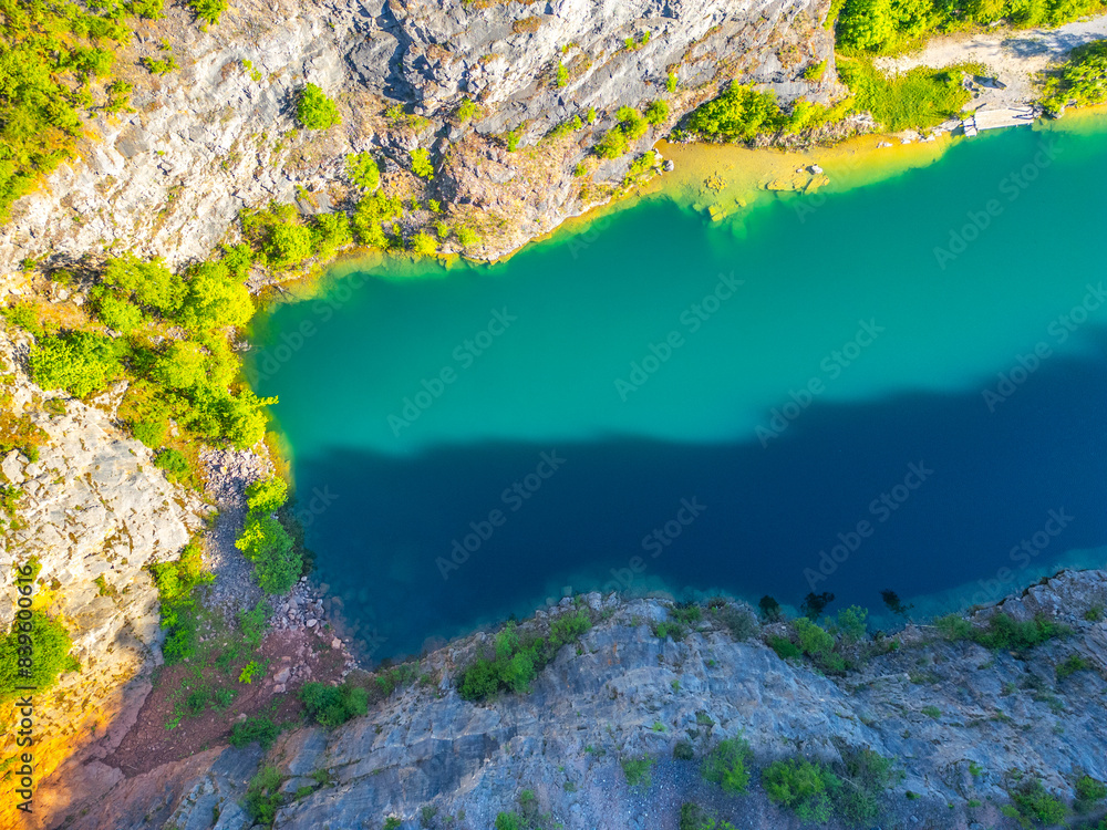 Obraz premium Beautiful aerial view of the abandoned Velka Amerika limestone quarry in Czechia, showcasing turquoise water and surrounding greenery in bright summer sunlight.