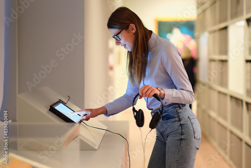 Woman wearing headphones and contemplates ancient arts. Student visiting gallery or museum. Concept of modern education and culture. photo