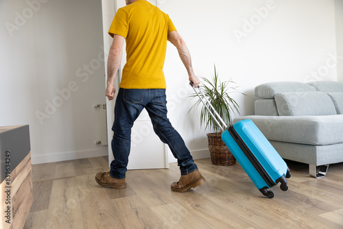 Foto young man leaving home with his blue wheeled suitcase to go on a trip
