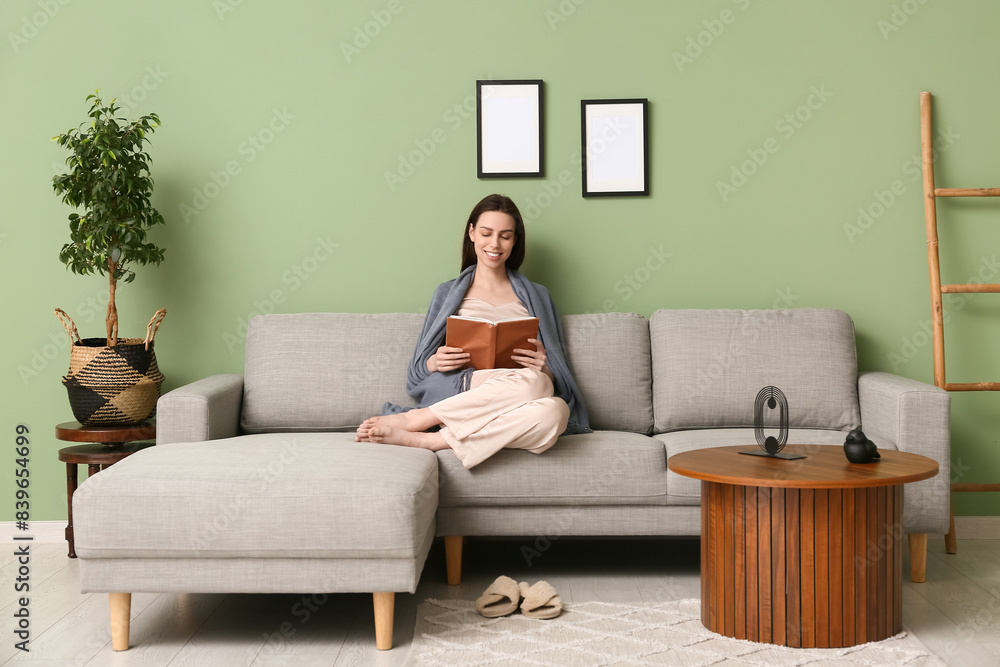 Young woman in pajamas and plaid reading book on sofa in living room Young woman in pajamas and plaid reading book on sofa in living room