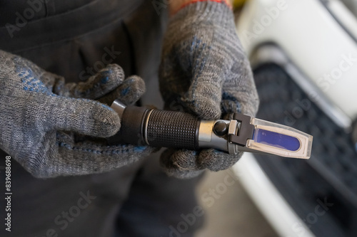 A mechanic holds a Refractometer in a car service center. Portable optical device for determining the freezing point of antifreeze.