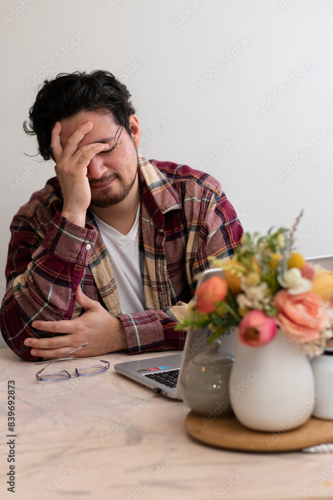 Young man with headache with his laptop in the living room making pain gesture Young man with headache with his laptop in the living room making pain gesture
