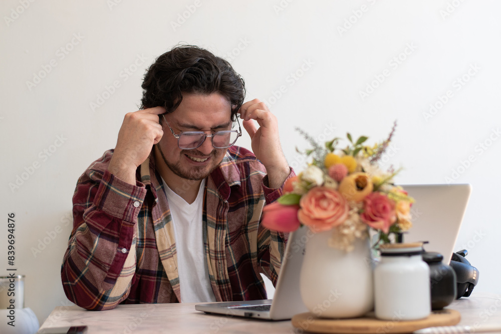 Young man with headache with his laptop in the living room making pain gesture Young man with headache with his laptop in the living room making pain gesture