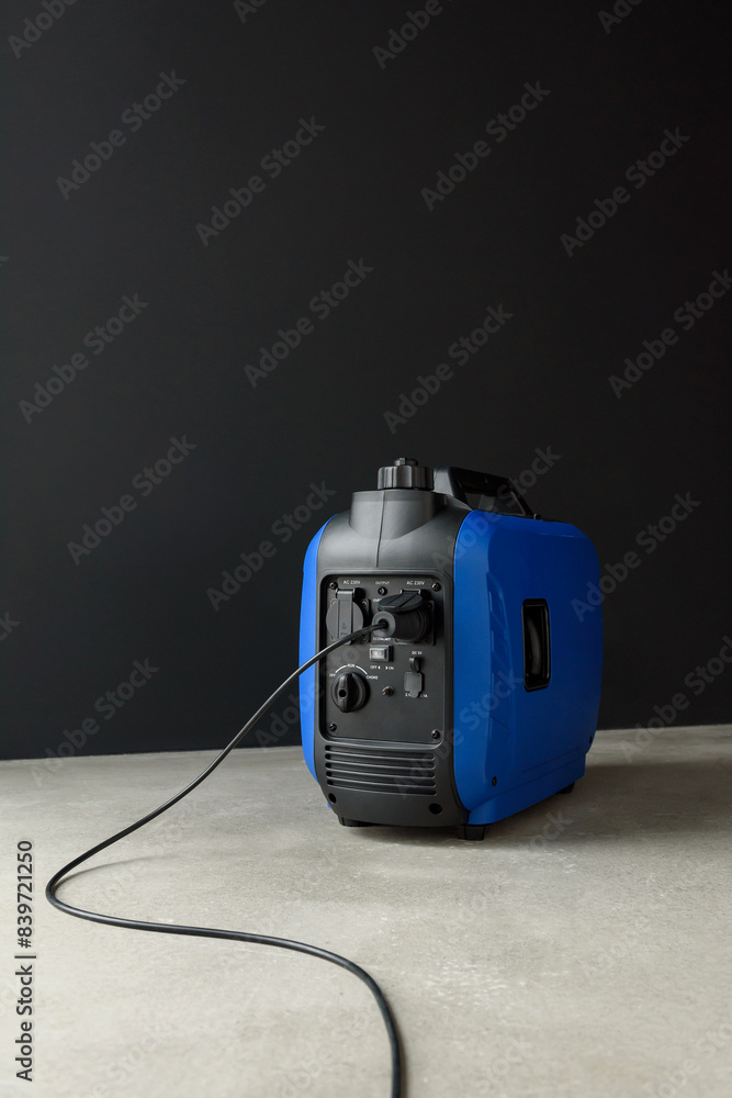 Connected generator. A modern blue portable gasoline inverter generator stands in a garage against a black wall. Backup autonomous power supply at home. Electricity production and generation. Connected generator. A modern blue portable gasoline inverter generator stands in a garage against a black wall. Backup autonomous power supply at home. Electricity production and generation.