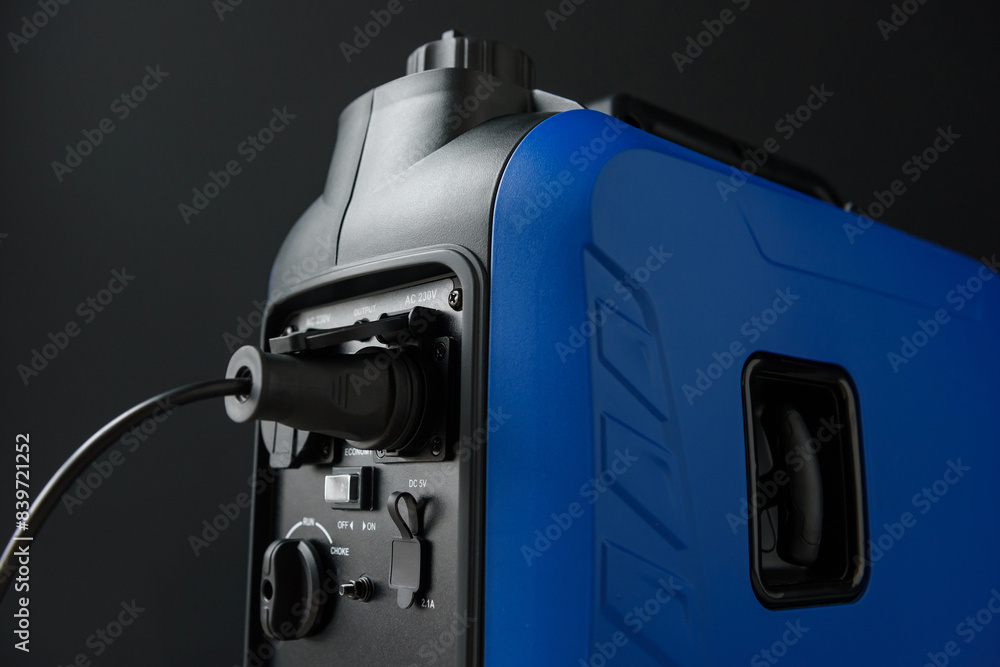 Close-up of the connected socket and generator ports. A modern portable gasoline inverter generator stands in a garage against a black wall. Backup autonomous power supply at home. Close-up of the connected socket and generator ports. A modern portable gasoline inverter generator stands in a garage against a black wall. Backup autonomous power supply at home.