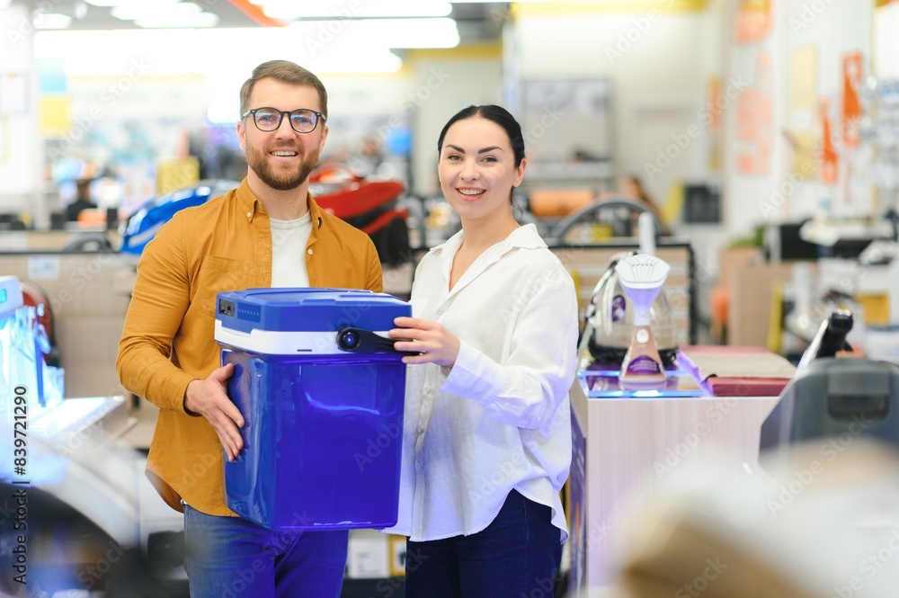 Obraz premium A young couple chooses a plastic cool box for outdoor recreation in an electronics store
