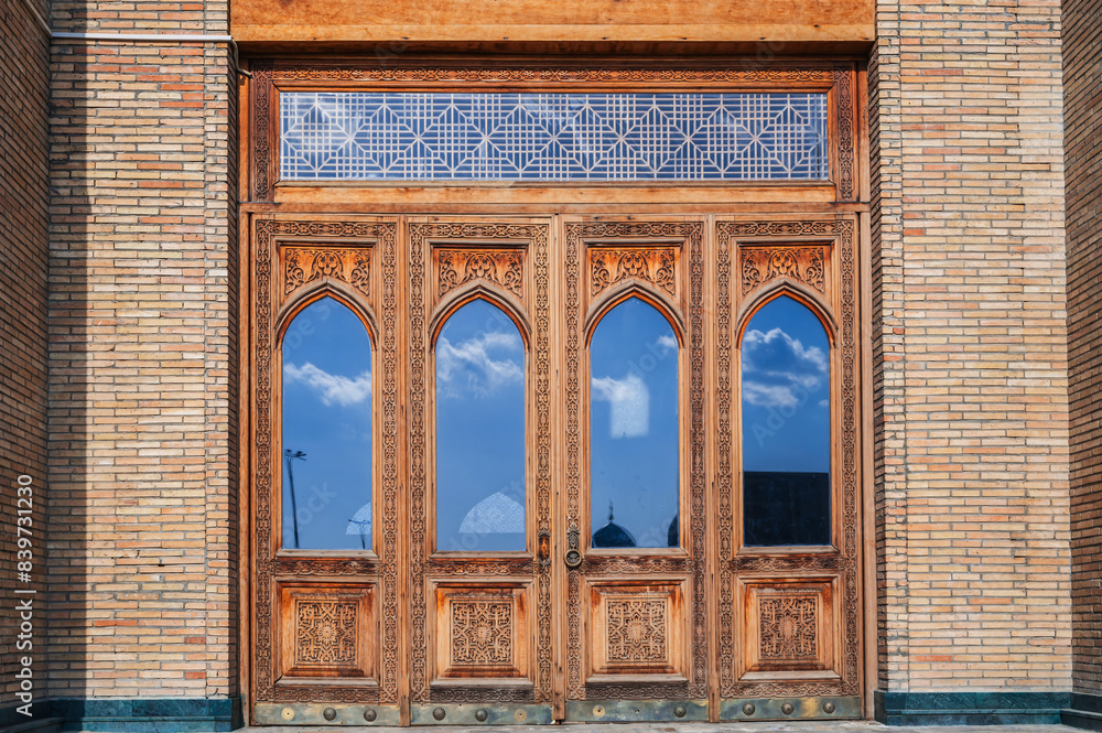 Obraz premium old carved wooden door with glass with Uzbek pattern to the ancient Islamic Mosque of Hazrati Imam in Uzbekistan
