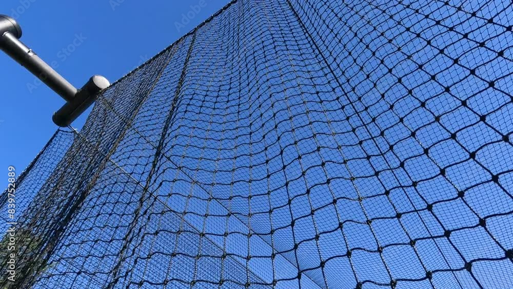 Sports Nets Against a Clear Blue Sky. Looking up a sports netting used to enclose a batting cage. The nets move with the wind in slow motion. Black net set against a clear blue sky. Sports Nets Against a Clear Blue Sky. Looking up a sports netting used to enclose a batting cage. The nets move with the wind in slow motion. Black net set against a clear blue sky.