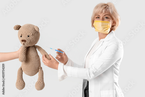 Female pediatrician in medical mask with vaccine and toy bear on white backgr...
