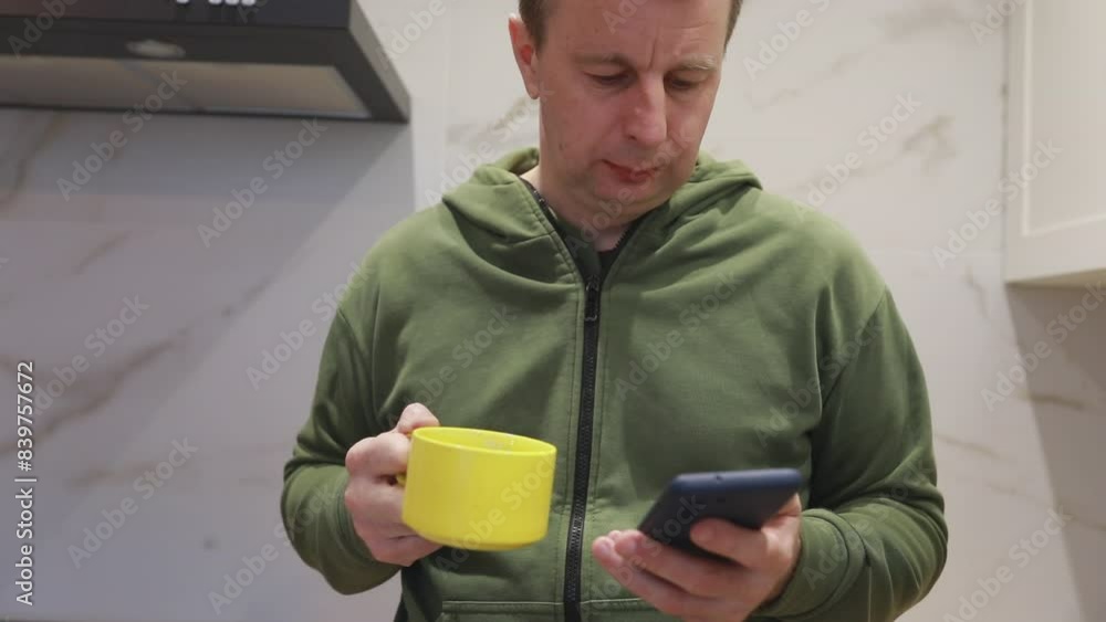 Man in Green Hoodie Using Smartphone While Drinking Coffee in a Modern Kitchen Man in Green Hoodie Using Smartphone While Drinking Coffee in a Modern Kitchen