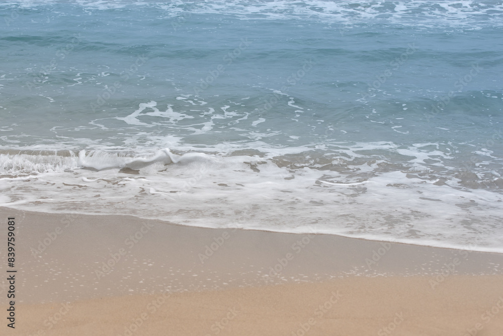 Background of waves flowing gently onto the beach. You can see the beach, the waves with foam and the blue sea. There is space for text. Background of waves flowing gently onto the beach. You can see the beach, the waves with foam and the blue sea. There is space for text.