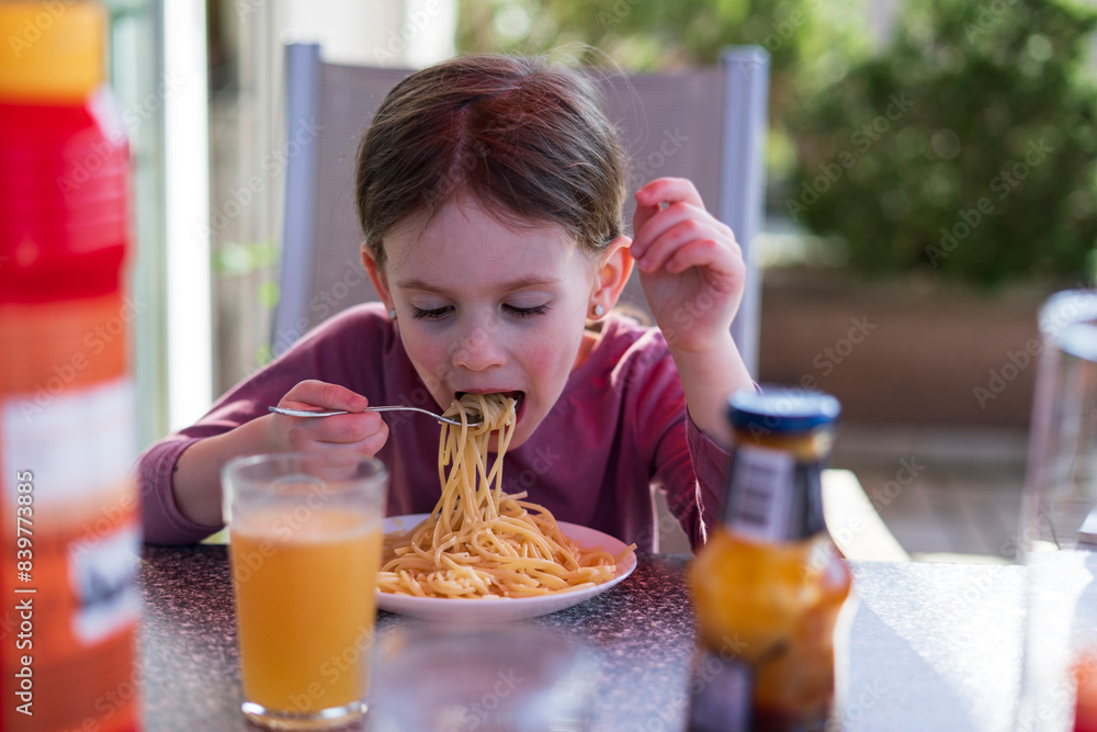 A little cute girl sits on the terrace of her house and eats pasta. Happy children's life concept A little cute girl sits on the terrace of her house and eats pasta. Happy children's life concept