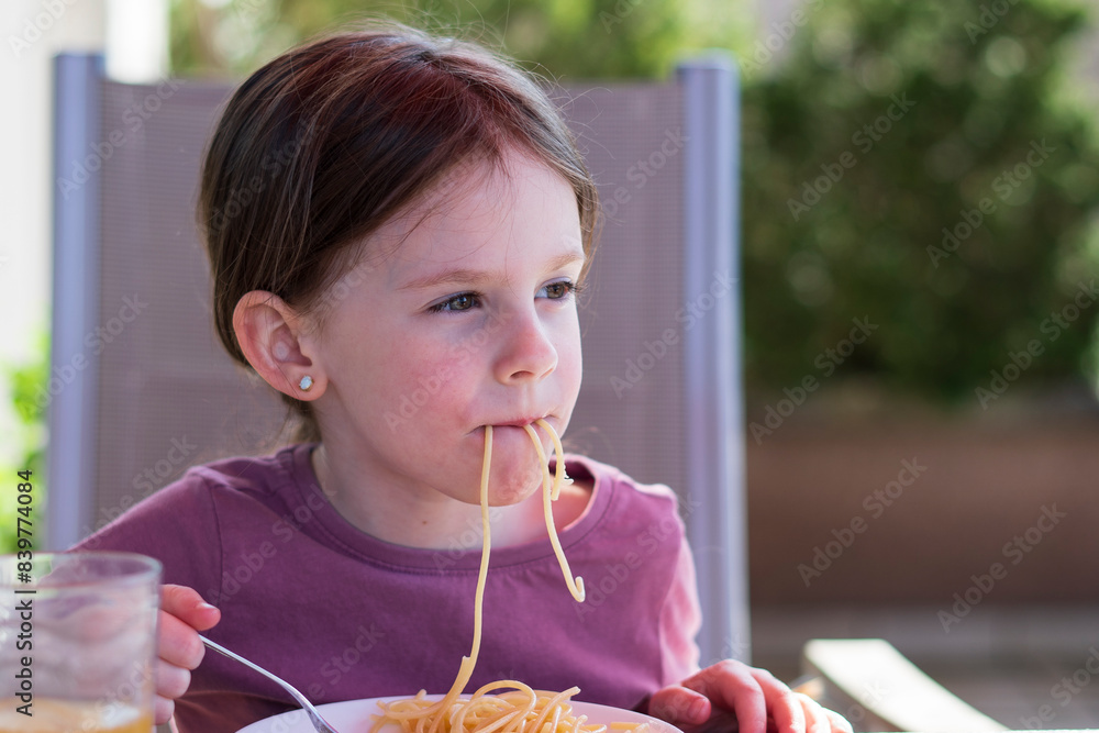 A little cute girl sits on the terrace of her house and eats pasta. Happy children's life concept A little cute girl sits on the terrace of her house and eats pasta. Happy children's life concept