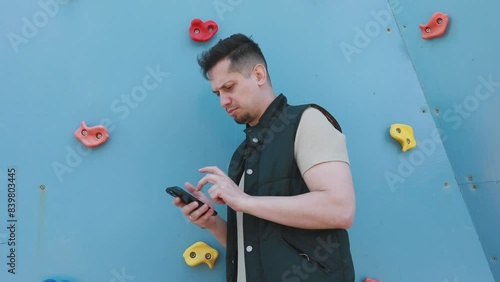 Man Standing in Front of Climbing Wall Using Cell Phone photo